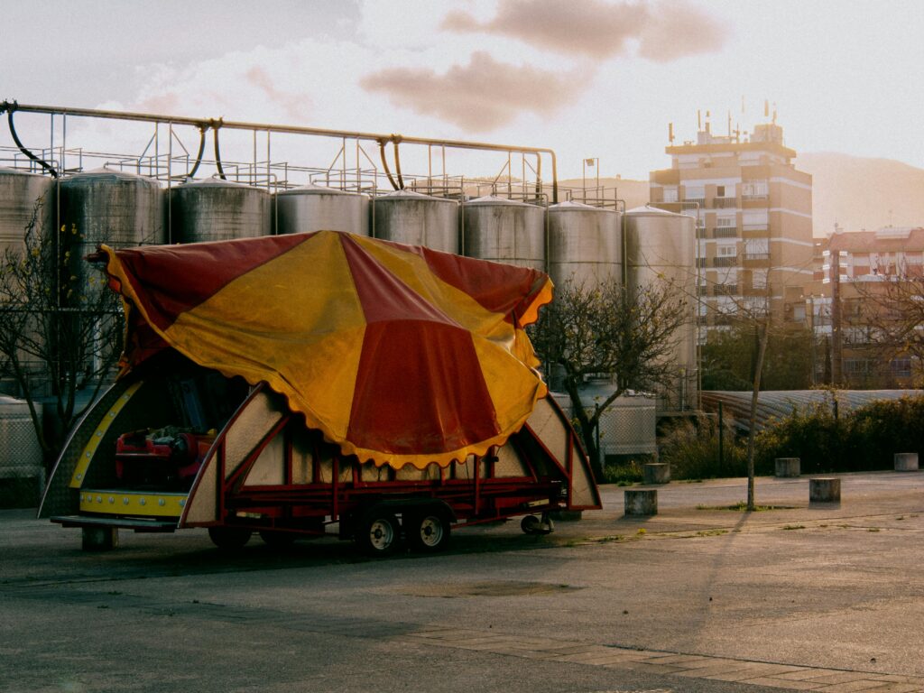 A colorful circus tent trailer parked at an industrial location during sunset.